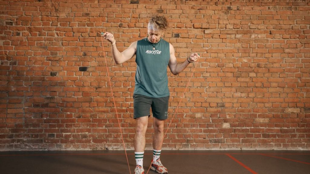 Caucasian man engaging in a jump rope workout in an indoor setting with a brick wall background.