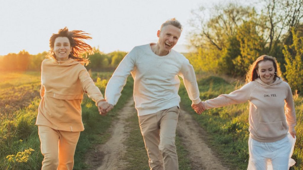 Delighted young friends holding hands while having fun while jumping towards at sunset